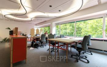 Office space rental at Zomerhofstraat 84 in Rotterdam North, featuring modern desks, chairs, and large windows with a leafy view.