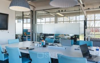 Interior of office space rental at Overschieseweg 34, Schiedam, featuring a meeting room with a long white table, blue chairs, multiple laptops and office supplies.