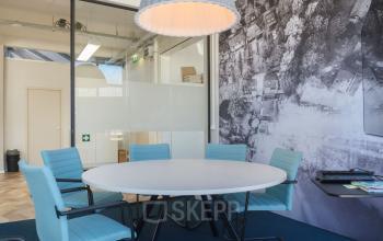 Furnished office space at Overschieseweg 34, Schiedam, with a round table, chairs, and a large wall mural.