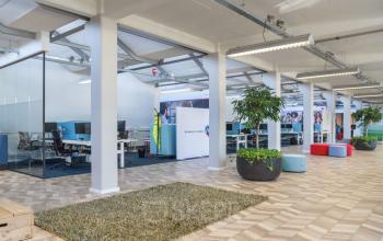 Modern open-plan office space at Overschieseweg 34, Schiedam with desks, glass partitions, and green plants.