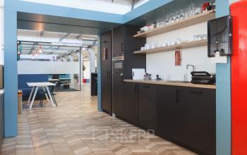 Modern kitchen area with black cabinets, wooden shelves, and stocked with kitchen appliances in an office building at Overschieseweg 34, Schiedam.