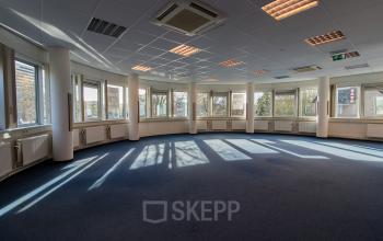 Spacious, well-lit office space with large windows and blue carpet at Noordvest 18, Schiedam, available for rent.