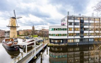 Exterior view of the office building at Noordvest 18, Schiedam, showing a distinctive windmill nearby and reflections on the canal.