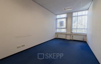 Empty office space with blue carpet and two windows at Noordvest 18, Schiedam, available for office space rental.