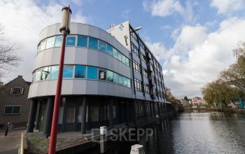 Modern office building located at Noordvest 18, Schiedam, with glass windows and curved architecture beside a canal.