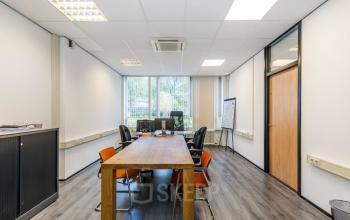 Bright office at Noordvest 18, Schiedam, featuring a central wooden table surrounded by chairs and desks, ideal for office space rental with natural light through large windows.