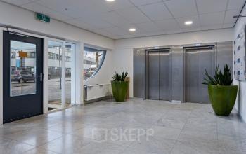 Spacious lobby area at De Brauwweg 52-66 in Schiedam featuring elevators and large windows, ideal for office space rental with easy accessibility and bright ambiance.