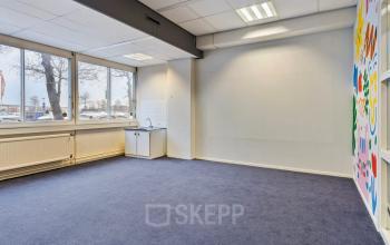 Interior view of an unfurnished office space for rent at De Brauwweg 52-66, Schiedam, featuring large windows and colorful wall art.
