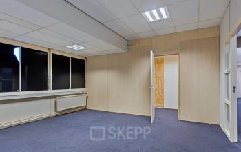 An unfurnished office interior at de Brauwweg 52-66 in Schiedam, ideal for those seeking office space rental. The room features carpeted floors and large windows providing natural light.