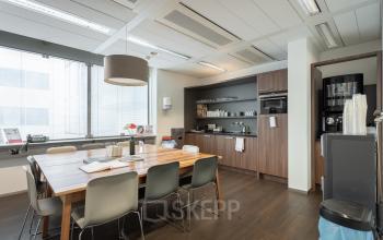 Furnished office space for rent at Schiphol Boulevard 127 with a wooden table, chairs, and a kitchenette area.
