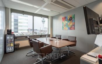 Furnished office space rental at Schiphol Boulevard 127 in Schiphol Airport, featuring a large table, chairs, and a view of the airport control tower.