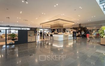 Modern office interior at Schiphol Boulevard 127 with an open lounge area and people engaging in business discussions. Ideal office space rental option featuring a chic café setup.