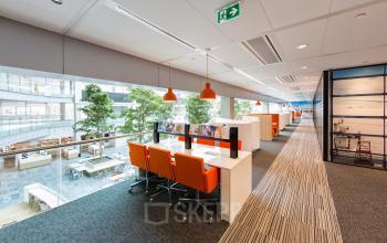 Modern office space rental at Evert van de Beekstraat 104, Schiphol, with vibrant orange chairs and sleek workstations.