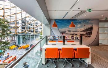 Modern lounge area at Evert van de Beekstraat 104, Schiphol, ideal for an office space rental with vibrant orange chairs and large windows.