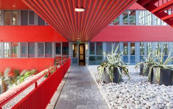 A vibrant red exterior hallway at Schiphol Airport's Folkstoneweg office to rent, featuring large potted plants and modern architectural design.