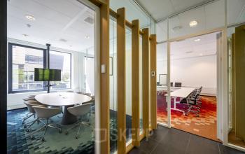 Modern conference room with a round table and chairs facing large windows and adjoining meeting rooms at Boeingavenue 223 – 239, Schiphol Rijk, Schiphol, highlighting office space rental options.