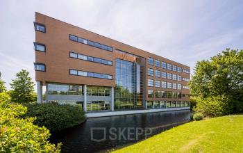 Exterior view of an office building at Boeing Avenue 1-19, Schiphol Rijk, ideal for office space rental with a modern facade next to a serene water body.