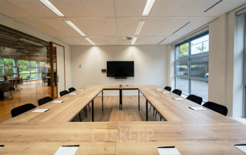 A bright conference room at Boeing Avenue 1-19, Schiphol Rijk, featuring a U-shaped wooden table, chairs, and a wall-mounted screen, ideal for office space rental.