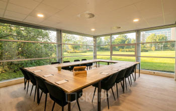 Spacious office with large windows overlooking greenery at Boeing Avenue 1-19, perfect for office space rental. Modern furnishings include a large table and chairs, ideal for meetings.