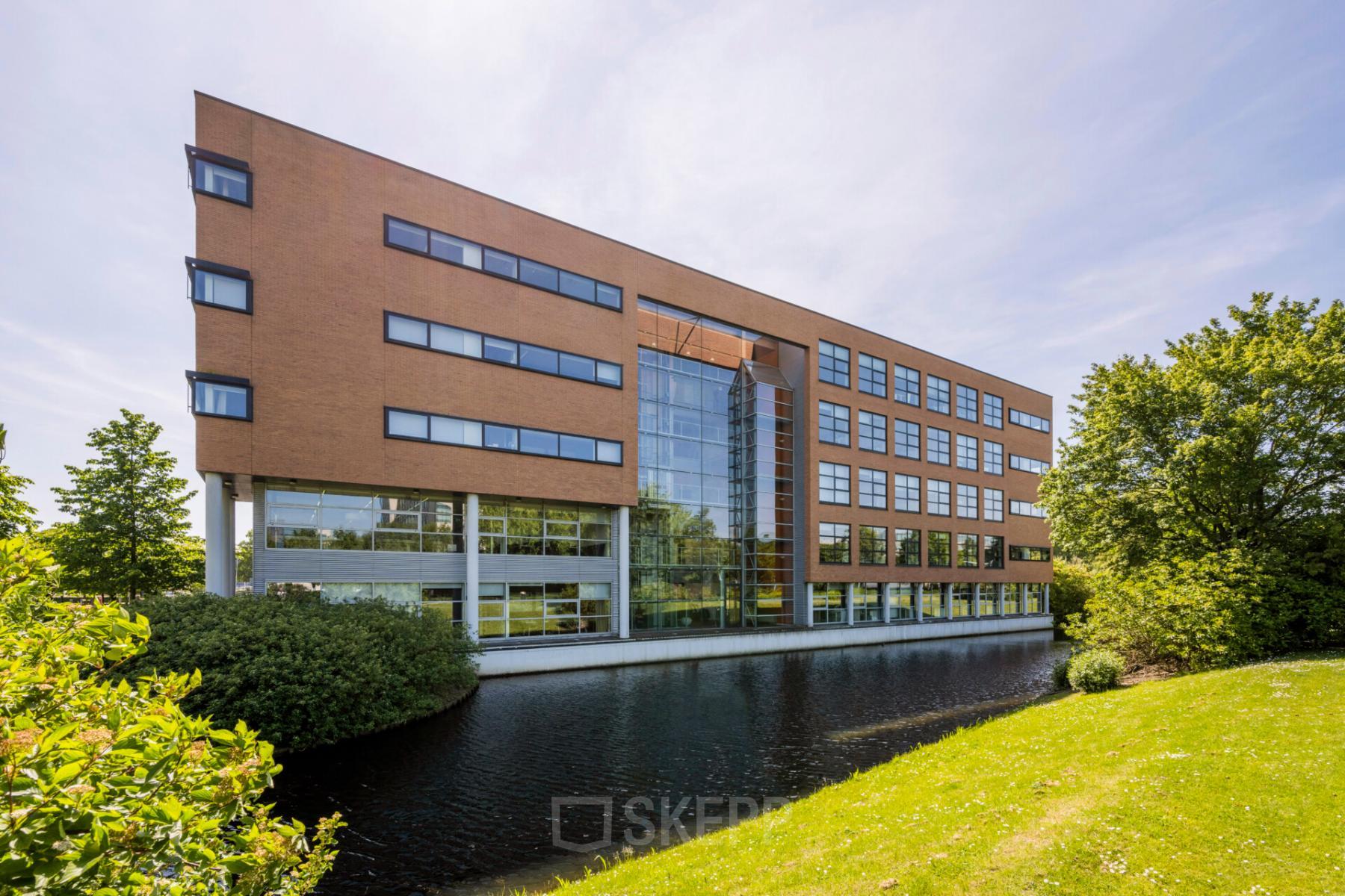Exterior view of an office building at Boeing Avenue 1-19, Schiphol Rijk, ideal for office space rental with a modern facade next to a serene water body.