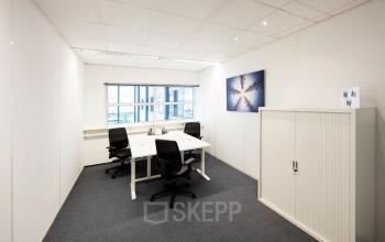 Modern office space with natural light located at Beechavenue 54-62, Schiphol Rijk, featuring white walls, a set of desks, chairs, and storage cabinet.