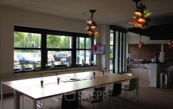 Bright and modern office space rental at Poststraat 8 in Sittard, featuring a large table with chairs and vibrant light fixtures.