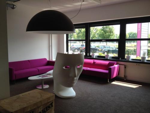Modern office space rental at Poststraat 8, Sittard with vibrant pink sofa, unique art installations, and ample natural light.