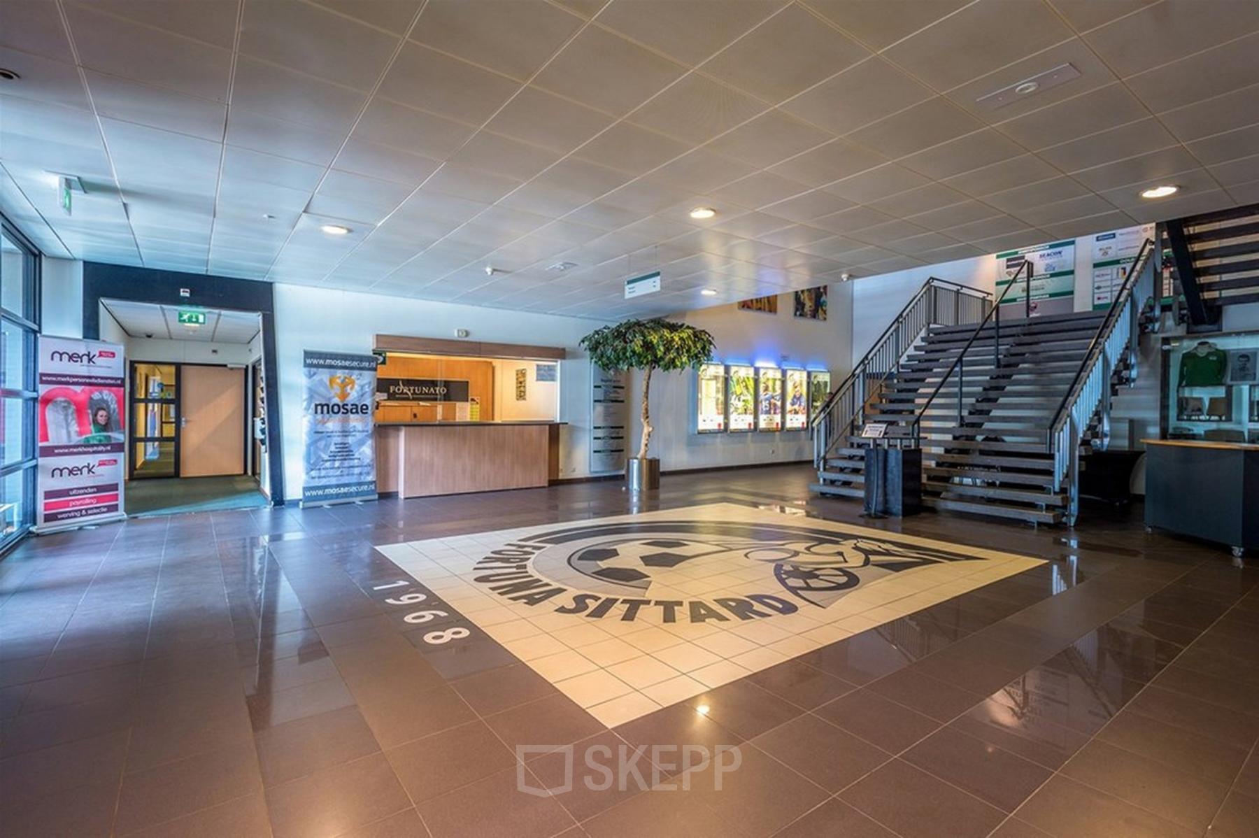 Spacious entrance area at 200 Milaanstraat, Sittard, showcasing a modern reception with a large logo on the floor, inviting as part of the office space rental offering.