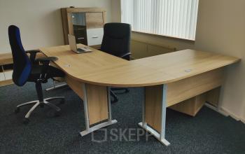 Furnished office space at Dr. Nolenslaan 157, Sittard, featuring modern wooden desks and chairs beside a large window.