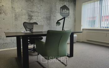 Office space rental at Dr. Nolenslaan 157 in Sittard, featuring a minimalist office with a desk, chairs, lamp, and laptop in a well-lit room.