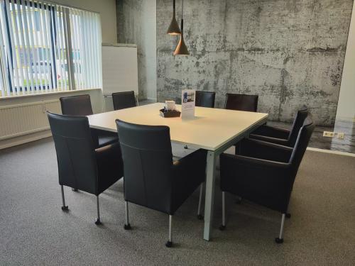 Modern conference room with a rectangular table surrounded by eight black chairs, located at Dr. Nolenslaan 157, Sittard. Concrete walls and large window enhance the spacious office space rental.