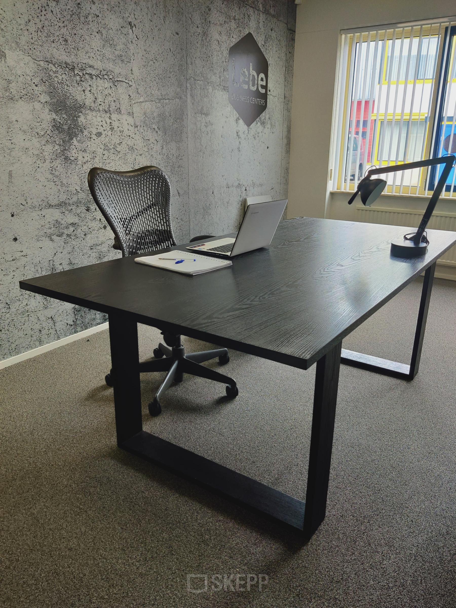 Modern office with a sleek black desk, ergonomic chair, laptop, and desk lamp at Dr. Nolenslaan 157, Sittard. Perfect for office space rental.
