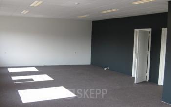 Spacious, unfurnished office space for rent at Nusterweg 63, Sittard, featuring carpeted floors and simple white and dark gray walls. Ideal for an office to rent setup.