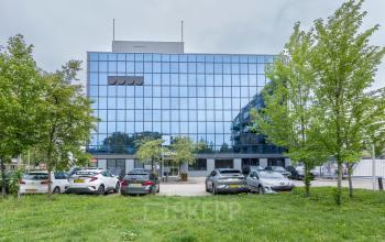 Exterior view of office space rental at Curieweg 9, Spijkenisse with a modern glass facade and parked cars in front.