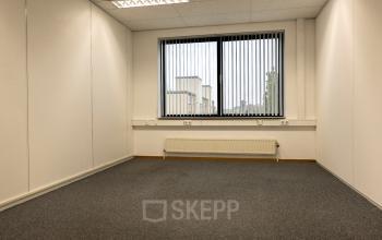 Empty office space at Curieweg 9, Spijkenisse, available for rent. The room features a window with vertical blinds and overhead fluorescent lighting.