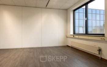 Empty office space with wooden flooring and a large window, available for rent at Curieweg 9, Spijkenisse.