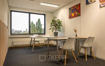 Bright office space with modern furniture at Curieweg 9, Spijkenisse, available for rent. Features large windows, a plant, and colorful artwork on the walls.