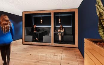 Moderne Arbeitskabinen in einem Büro in Königstraße 38, Stuttgart Mitte. Zwei Personen arbeiten an Laptops und besprechen geschäftliche Angelegenheiten.