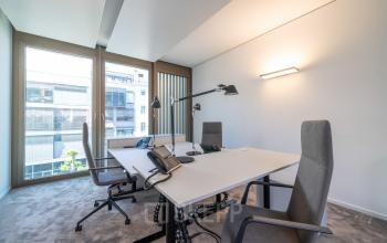 Moderner Büroraum mit großen Fenstern, einem Tisch mit Bürostühlen und Laptops, ideal für alle, die in Stuttgart Mitte eine Bürofläche mieten möchten.