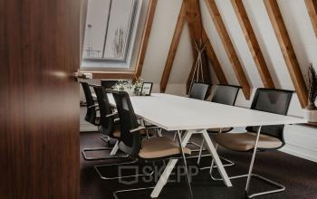 Cozy meeting room with A-frame beams and a long white table surrounded by black office chairs at Bredaseweg 8, ideal for office space rental in Terheijden, Breda.