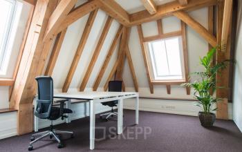 Modern office to rent at Bredaseweg 8, Breda Terheijden, showcasing wooden beams, two desks, chairs, and a potted plant under ample natural light.