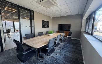 Bright and modern conference room available for office space rental in Tilburg, featuring a large wooden table, comfortable chairs, and a flat-screen TV.