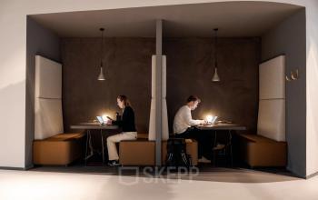 Two people working at individual booths with laptops at an office space rental, featuring a modern design at Daalsesingel 51, Utrecht Central Station.