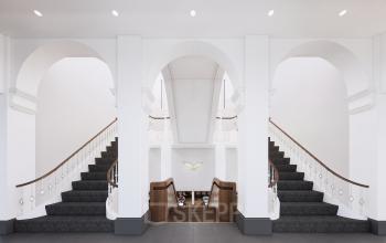 Grand dual staircase at Moreelsepark 1, leading to modern office space rental at Utrecht Central Station. Elegant white arches enhance the inviting atmosphere, ideal for business needs.