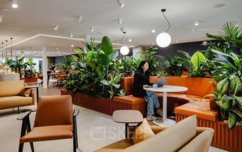 A modern office space rental at Moreelsepark 1, Utrecht Central Station, featuring stylish seating and greenery, with a person working on a laptop.