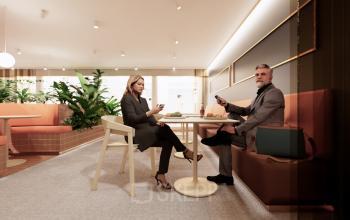 Modern office interior at Moreelsepark 1, Utrecht Central Station, featuring comfortable seating and natural decor. Two professionals engage in a business conversation, perfect for office space rental.