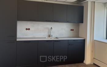 Modern pantry area in an office space at Jaarbeursplein 22, featuring sleek black cabinets and a stainless steel sink, perfect for office space rental.