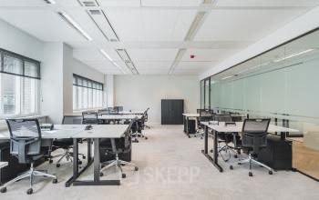 Modern office with glass partitions at Leiden Central Station for rent, featuring ergonomic chairs and ample desk space.