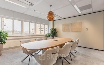 Bright, modern office with large windows and a central meeting table surrounded by chairs, located at Leidseveer 2-10, Utrecht Central Station. Ideal office space rental for productive meetings.