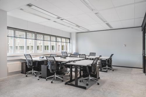Modern furnished office space with multiple desks and chairs, located at Leidseveer 2-10, Utrecht Central Station, ideal for rent office space. Natural light fills the room through large windows.